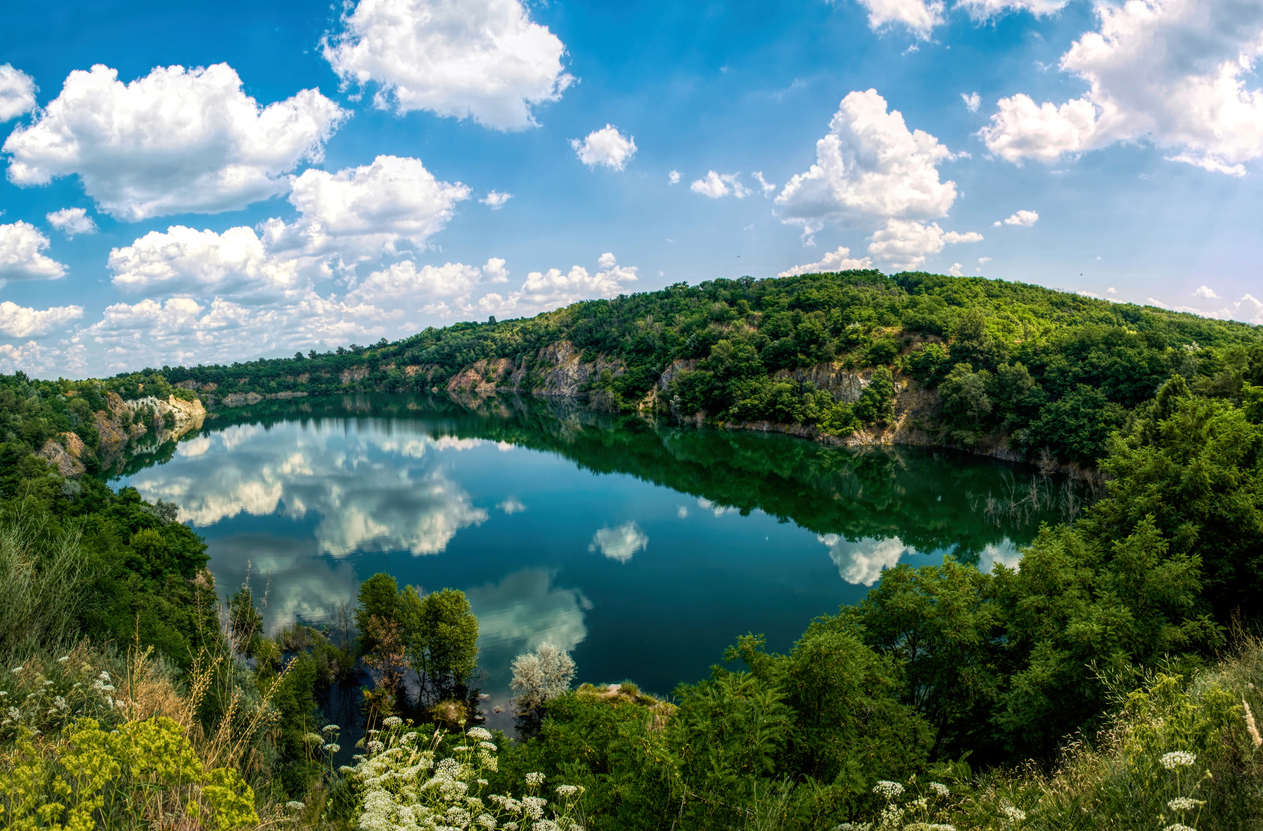 Scenic summer landscape in New England, USA. An old abandoned quarry, flooded with water. A lake with rocky shores with a blue sky reflected in the water surface. Summer travel to the northeastern USA