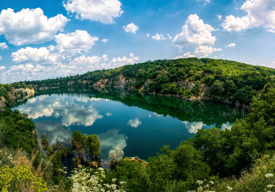 Scenic summer landscape in New England, USA. An old abandoned quarry, flooded with water. A lake with rocky shores with a blue sky reflected in the water surface. Summer travel to the northeastern USA